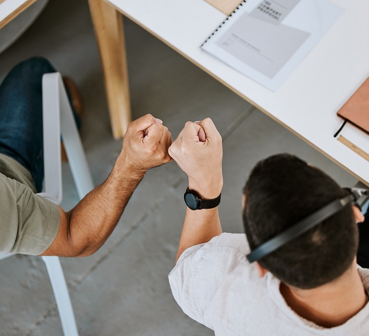 Twee collega's geven elkaar een boks aan een bureau